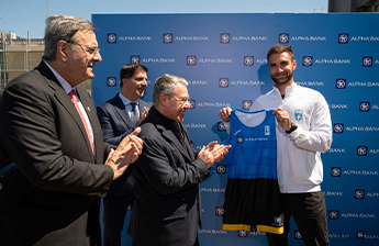 Οι Ισίδωρος Κούβελος, Βασίλης Πολύμερος, Βασίλης Ψάλτης συγχαίρουν αθλητή που κρατά στολή κωπηλασίας με λογότυπο Alpha Bank.