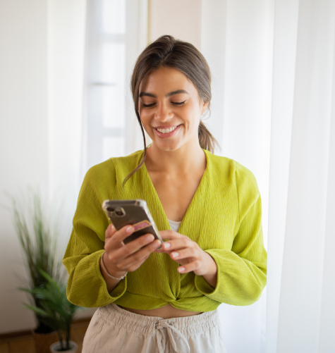 Γυναίκα που κρατάει κινητό, το κοιτάει και χαμογελάει